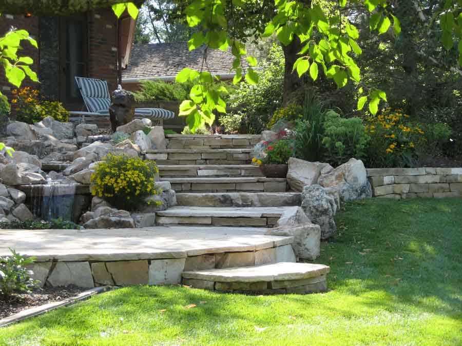 Flagstone terrace and steps with boulders and yellow flowers beside a lawn